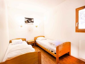 A small, single room with two wooden beds, a small table, and a wall-mounted light fixture. - Bright apartment with valley view - 6 guests (Villarodin-Bourget)