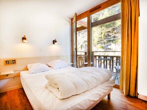 A bedroom with a large bed, two wall-mounted lights, a wooden headboard, and a balcony with a view of trees and a rocky landscape. - Bright apartment with valley view - 6 guests (Villarodin-Bourget)