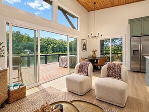 A spacious room with a large sliding glass door leading to a deck, a dining area with a table and chairs, and a kitchen with a refrigerator. - Lakehaus at Water Edge -Modern Luxury/Beach/Dock/Kayaks/Fire Pit (Tracy City)