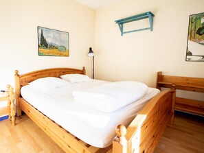 A wooden bed with white linens in a room with a wooden floor, a nightstand, a lamp, and two paintings on the walls. - Apartment, pets welcome - mountain view (Villarodin-Bourget)