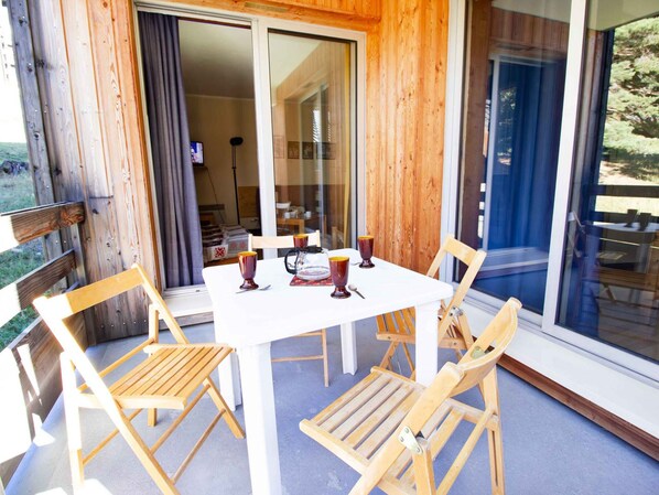 Een houten terras met een tafel en stoelen, een schuifpui en uitzicht op de omgeving.