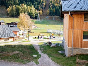 A rural setting with a wooden building, a clear path, and a fenced area with a playground. - Apartment, pets welcome - mountain view (Villarodin-Bourget)