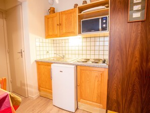 Eine kleine Küche mit Holzschränken, einem weißen Kühlschrank, einer Mikrowelle und einer gefliesten Spritzschutzwand.