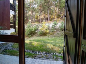 Blick aus einem Gebäude auf eine bewaldete Landschaft mit einem steinernen Weg, der zu einer Holztür führt.