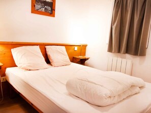Ein ordentlich bezogenes Bett mit weißer Bettwäsche und Kissen, ein Holz-Kopfteil, ein Nachttisch mit Lampe und eine Heizung.