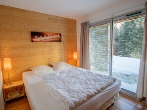A bedroom with a wooden headboard, a bed with white bedding, two bedside lamps, and a view of a snowy landscape through a glass door. - Chalet with pets, mountain view - 10 guests (Villarodin-Bourget)