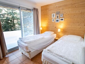 Camera d'albergo con due letti, parete in mattoni, pannelli in legno e un balcone con vista sugli alberi.