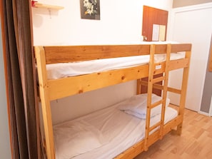 Ein Stockbett mit Holzrahmen, weißer Bettwäsche und einem kleinen Regal darüber.