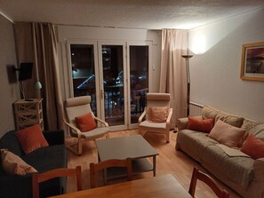 Ein Wohnzimmer mit einer Couch, Sesseln, einem Tisch und Blick durch eine Glastür nach draußen.