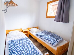 A small, single-room accommodation with two wooden beds, a wooden nightstand, and a window with curtains. - 3-room apartment, pets welcome, mountain view - 8 guests (Valfréjus)