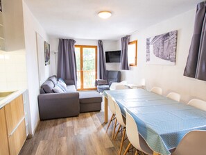 A modern living room with a sofa, a dining table with chairs, a TV, and a balcony with curtains. - 3-room apartment, pets welcome, mountain view - 8 guests (Valfréjus)