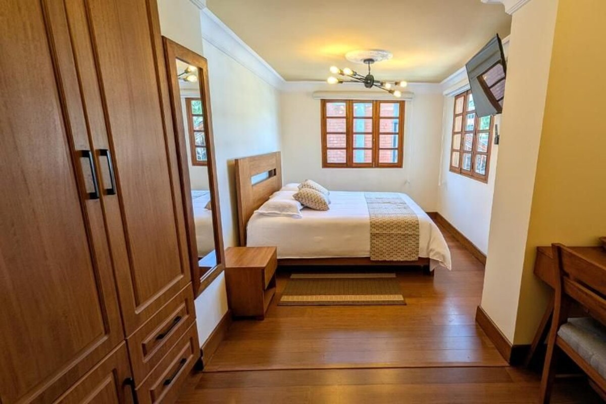 Ein Schlafzimmer mit einem hölzernen Bett, einem Nachttisch, einer Holzbank und einem Fenster mit Blick.