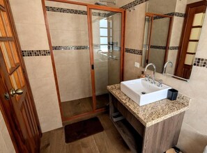 Une salle de bain avec une douche à parois de verre, un lavabo doté d’un plan de travail en granit et une porte en bois.