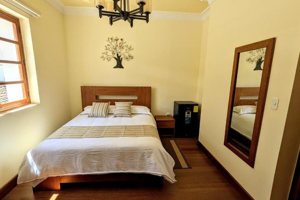 Ein Schlafzimmer mit Bett, Nachttisch, Spiegel, einer Chandelüster und einer Wanddekoration mit Baummotiv.