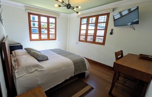 A bedroom with a bed, a desk, a TV, and two windows with wooden frames. - La Casona Emma Rooms (Quito)