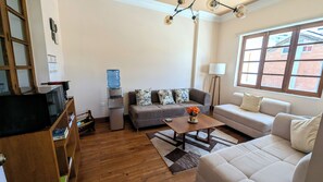 A living room with a sofa, a coffee table, a water dispenser, a television, and a window with a view of buildings. - La Casona Emma Rooms (Quito)