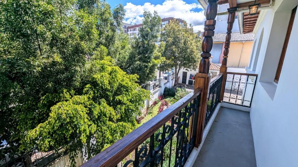 A balcony with a wooden railing and a view of lush greenery and buildings in the background.