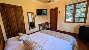 Ein Schlafzimmer mit einem Bett, einem Schreibtisch, einem Sessel, einem Fernseher und einem Fenster.