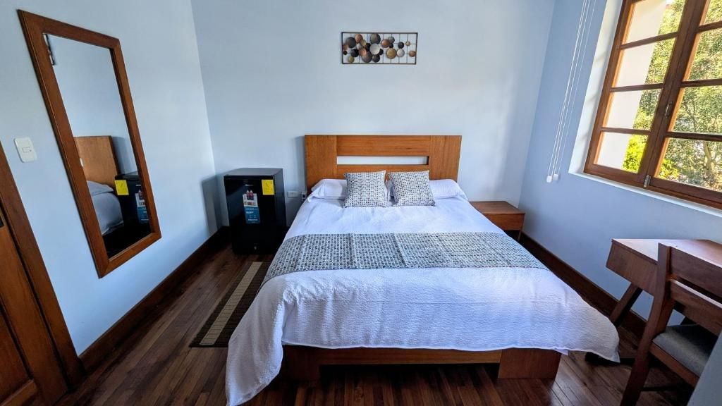 Un dormitorio con cama de madera, un escritorio, una silla, un espejo y una obra de arte en la pared.