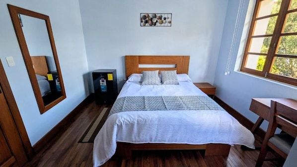 A bedroom with a wooden bed, a desk, a chair, a mirror, and a wall-mounted artwork. - La Casona Emma Rooms (Quito)
