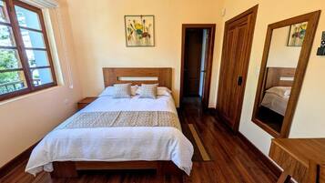 Un dormitorio con una cama de madera, una ventana, una puerta y un espejo.