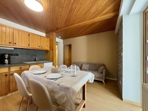 A dining area with a table set for four, wooden cabinets, a kitchen area, and a sofa. - Cozy apartment, 6 guests, peaceful location (La Salle-les-Alpes)