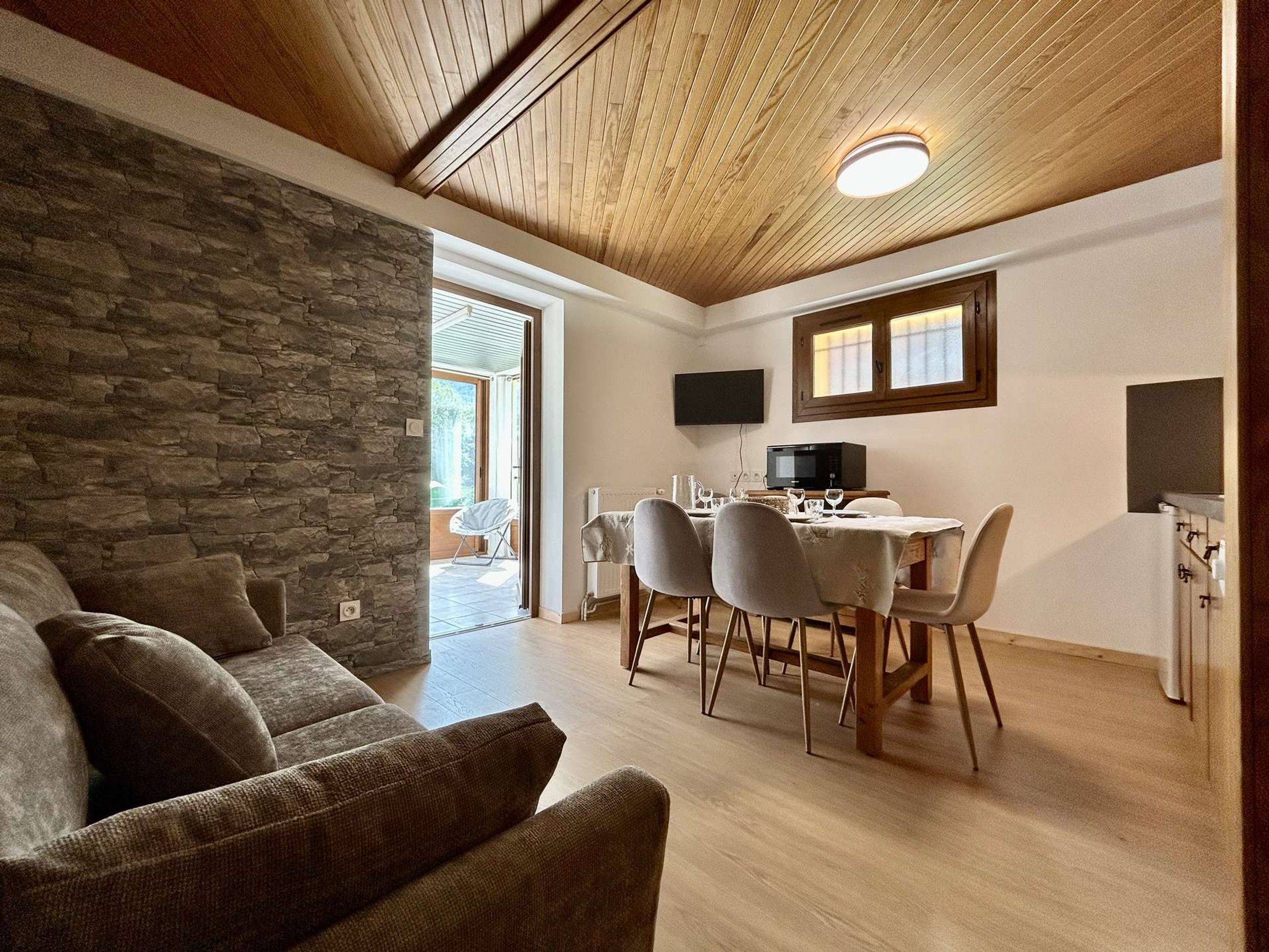 Ein gemütliches Wohnzimmer mit Steinwand, Holzboden und einer Essecke mit Tisch und Stühlen.