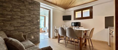 Un salon chaleureux avec un mur en pierre, un plafond en bois et un coin repas comprenant une table et des chaises.