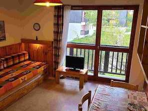 A cozy room with a wooden sofa, a television on a small table, and a large window with a view of greenery outside. - Charming apartment at the foot of the slopes - 4 guests (Villarodin-Bourget)