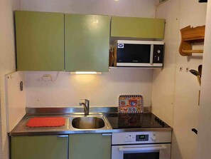 A compact kitchen with green cabinets, a microwave, a stove, and a sink. - Charming apartment at the foot of the slopes - 4 guests (Villarodin-Bourget)