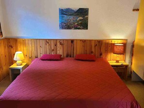 A room with a wooden headboard, a bed with red bedding, two pillows, a nightstand with a lamp, and a painting on the wall. - Charming apartment at the foot of the slopes - 4 guests (Villarodin-Bourget)