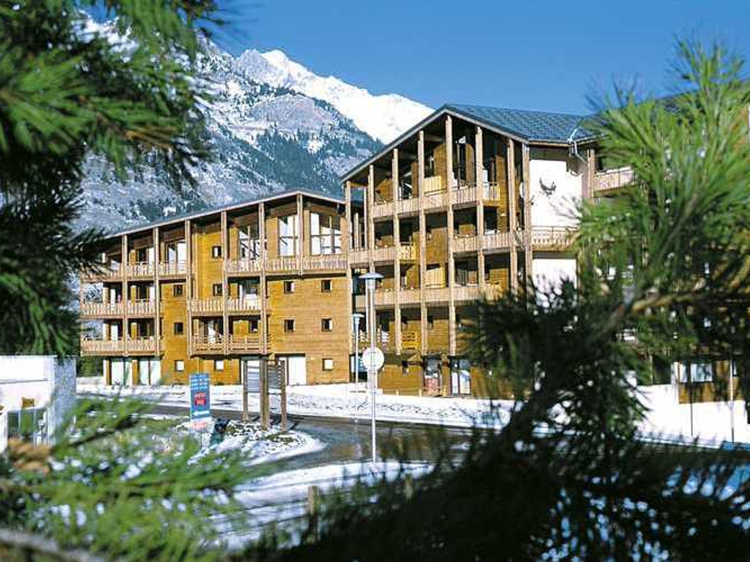 A multi-story building with balconies, a mountain backdrop, and a clear sky.
