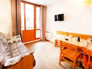 A room with a sofa, a dining table with chairs, a television mounted on the wall, and a window with curtains. - Studio mountain view, pets welcome - 3 guests (Valfréjus)