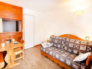A cozy room with a wooden table, a sofa with patterned cushions, and a wall-mounted light fixture. - Studio mountain view, pets welcome - 3 guests (Valfréjus)