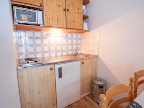 Una cucina compatta con pensili in legno, un forno a microonde integrato e un lavello.