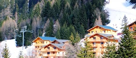 A cluster of wooden mountain lodges with multiple balconies, surrounded by dense forest and snow-covered slopes.