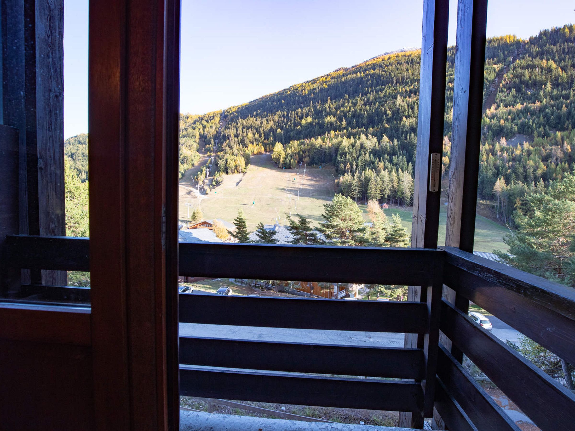 A wooden balcony with a view of a forested hillside and a clear sky.