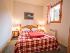 Ein Schlafzimmer mit einem Bett, zwei Nachttischlampen, einem Fenster mit Vorhängen, einem Wandbild und einem Heizkörper.