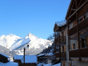 Ein Bergdorf mit Holzhäusern, ein schneebedeckter Berg im Hintergrund und ein klarer Himmel.