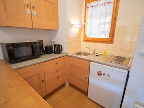 Eine kompakte Küche mit Holzschränken, einer Mikrowelle, einem Toaster, einer Spüle und einem Kühlschrank.