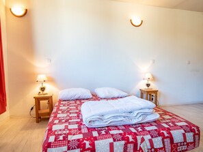 Ein ordentlich bezogenes Bett mit einer rot-weißen Steudecke, zwei Nachttischlampen und einem kleinen Nachttisch mit einer Lampe.