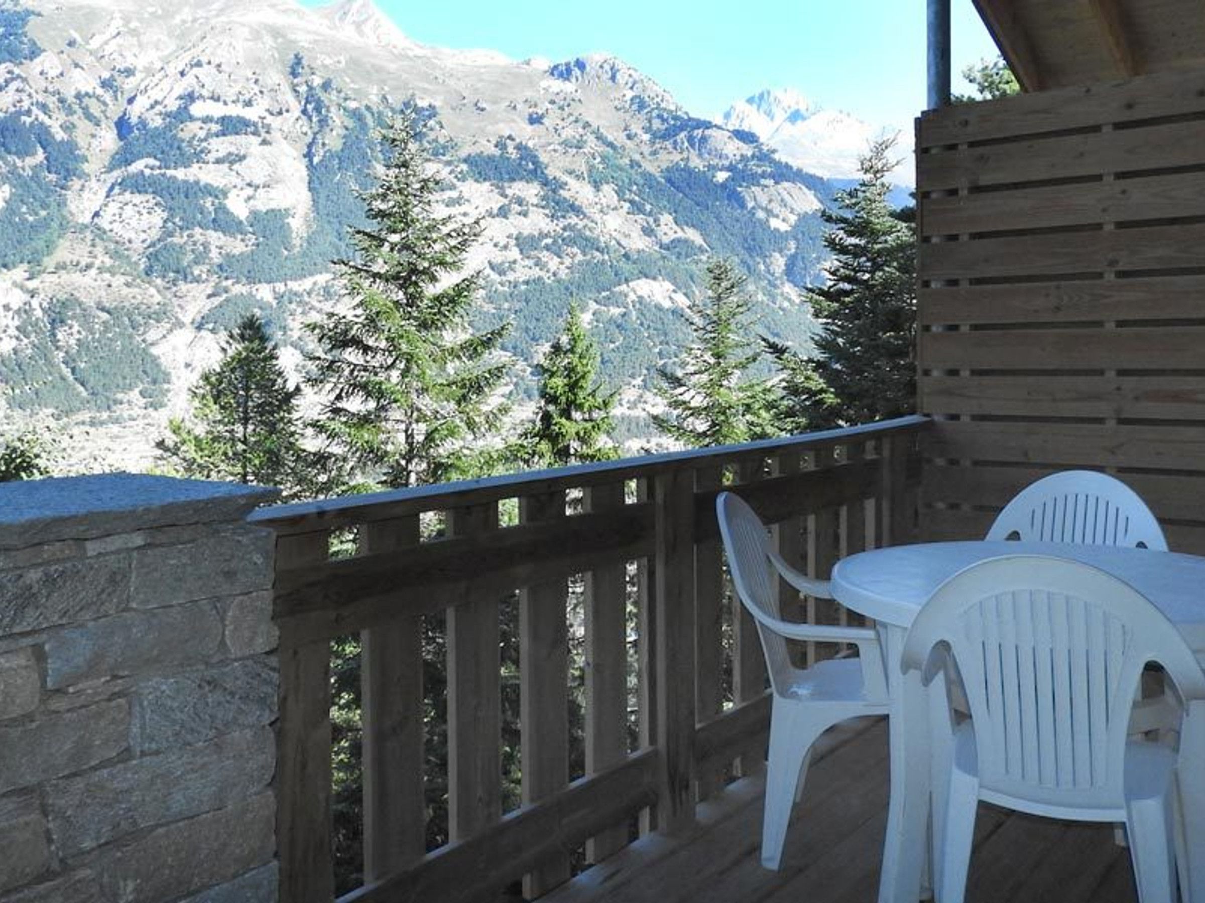 Un balcone con ringhiera in legno, sedie in plastica bianca e un tavolo.