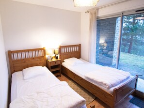A room with two wooden beds, a nightstand with a lamp, and a window with a view of trees. - Half-chalet, WiFi, pets welcome - 6 guests. Mountain view (Villarodin-Bourget)