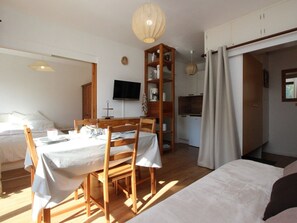 A room with a dining table, chairs, a television, a bookshelf, and a kitchen area. - 2-room apartment with balcony - 4 guests (Villarodin-Bourget)