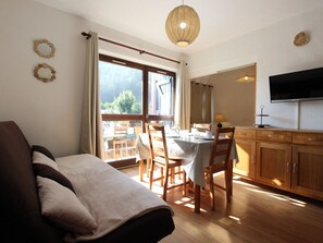 Een kamer met een bank, eettafel, stoelen, een televisie en een groot raam met gordijnen.