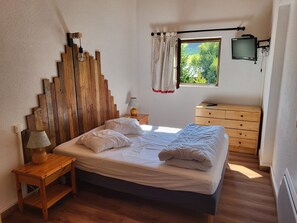 A bedroom with a wooden headboard, a bed with pillows and a blanket, a bedside table with a lamp, a dresser, and a window with a view of greenery. - Welcoming apartment, pets OK - 8 guests - Slope view (Villarodin-Bourget)