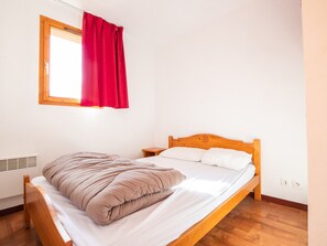Ein Einzelbett mit Holzrahmen und Kopfteil, ein roter Vorhang, ein weißes Kopfkissen und eine beige Decke.