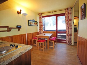 A kitchen with a wooden table and bench, a stove, and a window with curtains. - Charming apartment, mountain view - 4 guests (Villarodin-Bourget)