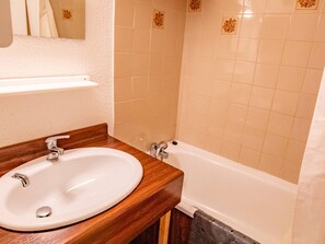 Ein Badezimmer mit einem Holzkosmetikschrank, einer weißen Spüle und einer Badewanne.