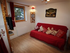 Ein gemütliches Zimmer mit einem roten Sofa, einer Holzleiter, einem fenster mit Vorhängen, einer Wandlampe und einem gerahmten Bild.
